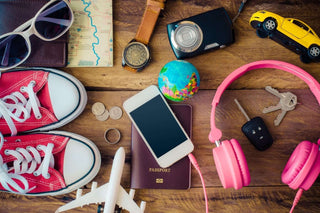 Flat lay of travel essentials: red sneakers, smartphone, passport, keys, globe, camera, money coins, map, and headphones.