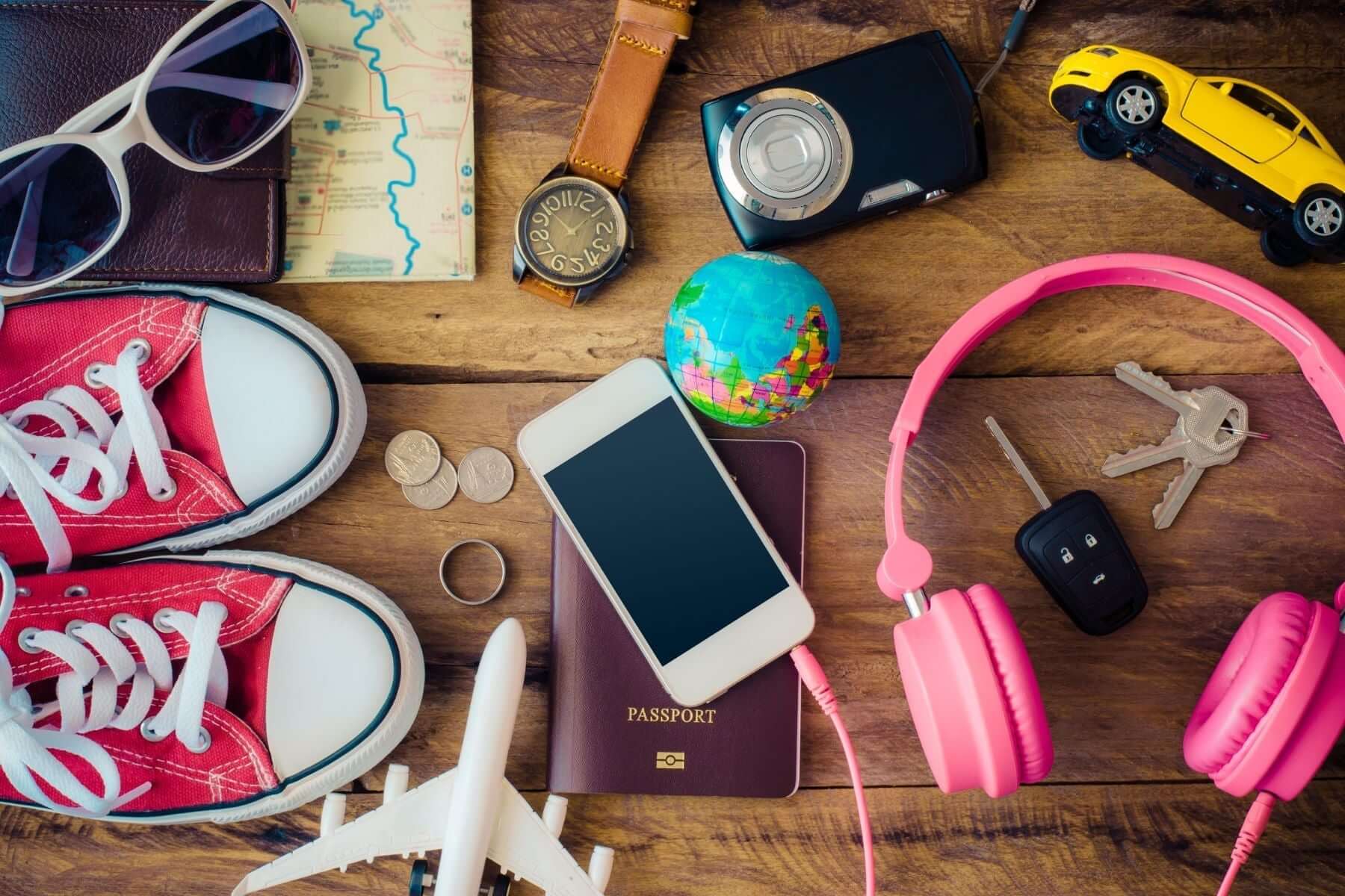 Colorful travel essentials including sneakers, headphones, passport, and camera arranged on a wooden surface.