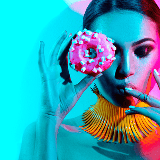 Woman holding a pink donut, showcasing vibrant fashion and colorful lighting for a trendy, modern aesthetic.