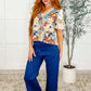 Model wearing a Less Concerned V-Neck Floral Blouse with colorful floral patterns and ruffle sleeves paired with navy trousers.
