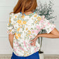Back view of a woman wearing a floral blouse with ruffle sleeves, featuring a v-neckline and vibrant colors.