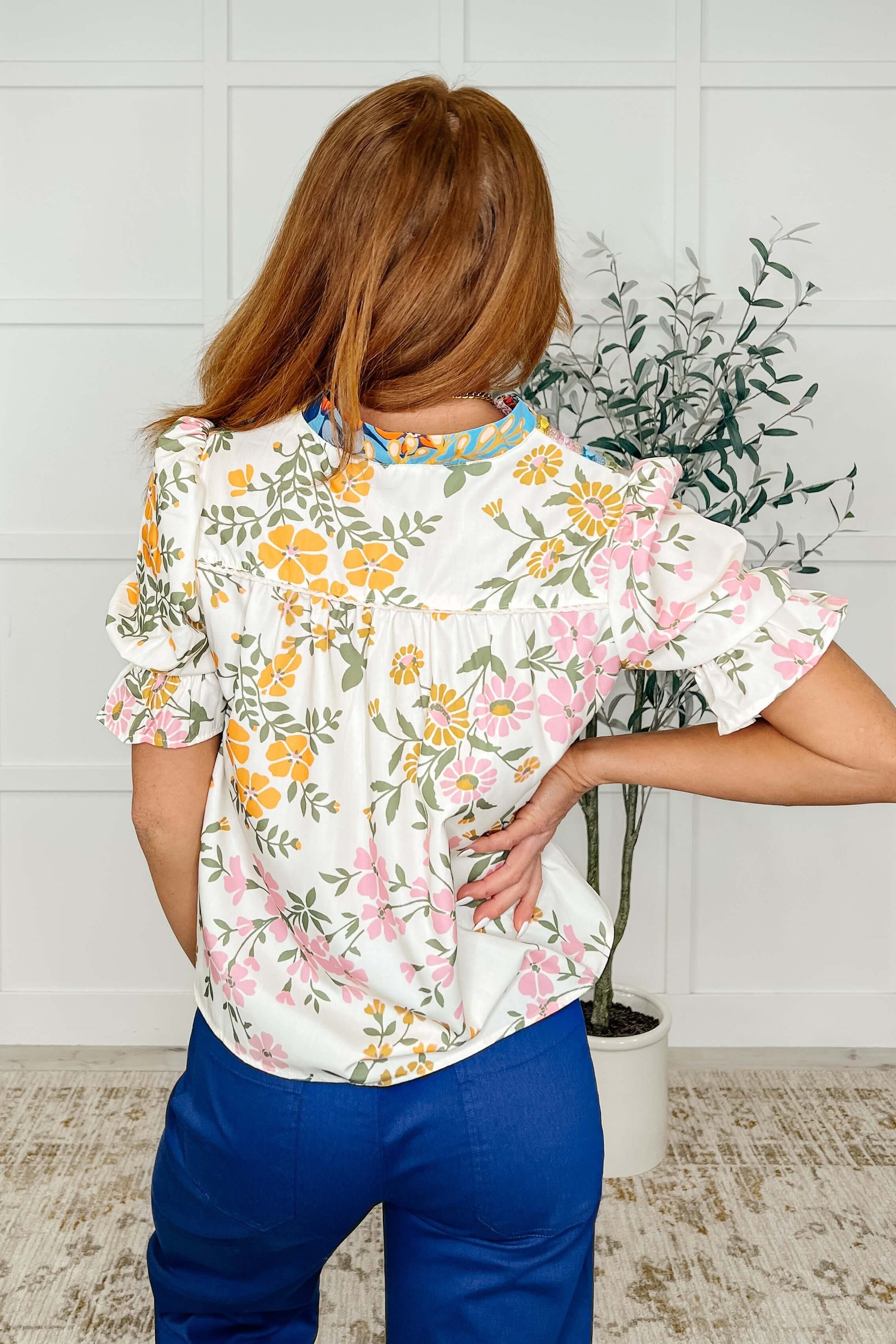 Back view of a woman wearing a floral blouse with ruffle sleeves, featuring a v-neckline and vibrant colors.