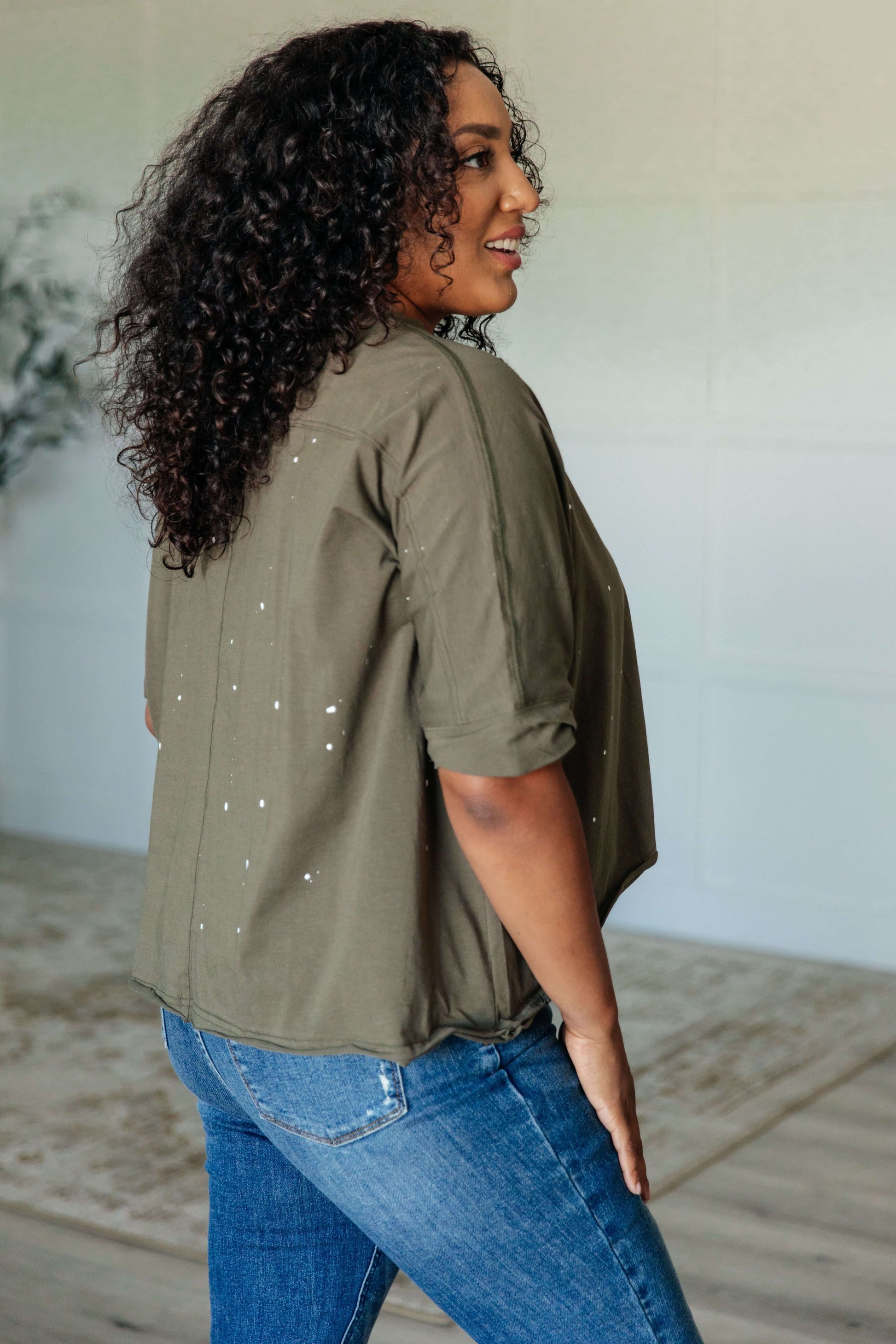 Model showcasing the Less Than Stressed Asymmetrical Distressed Top in olive green, featuring a unique design and relaxed fit.