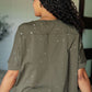 Back view of a woman in a distressed green top with paint splatter details and short sleeves, showcasing an asymmetrical hemline.