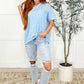 Model wearing the Layback Relaxed Basic Tee in light blue, paired with ripped jeans and white sneakers, standing next to a potted plant.